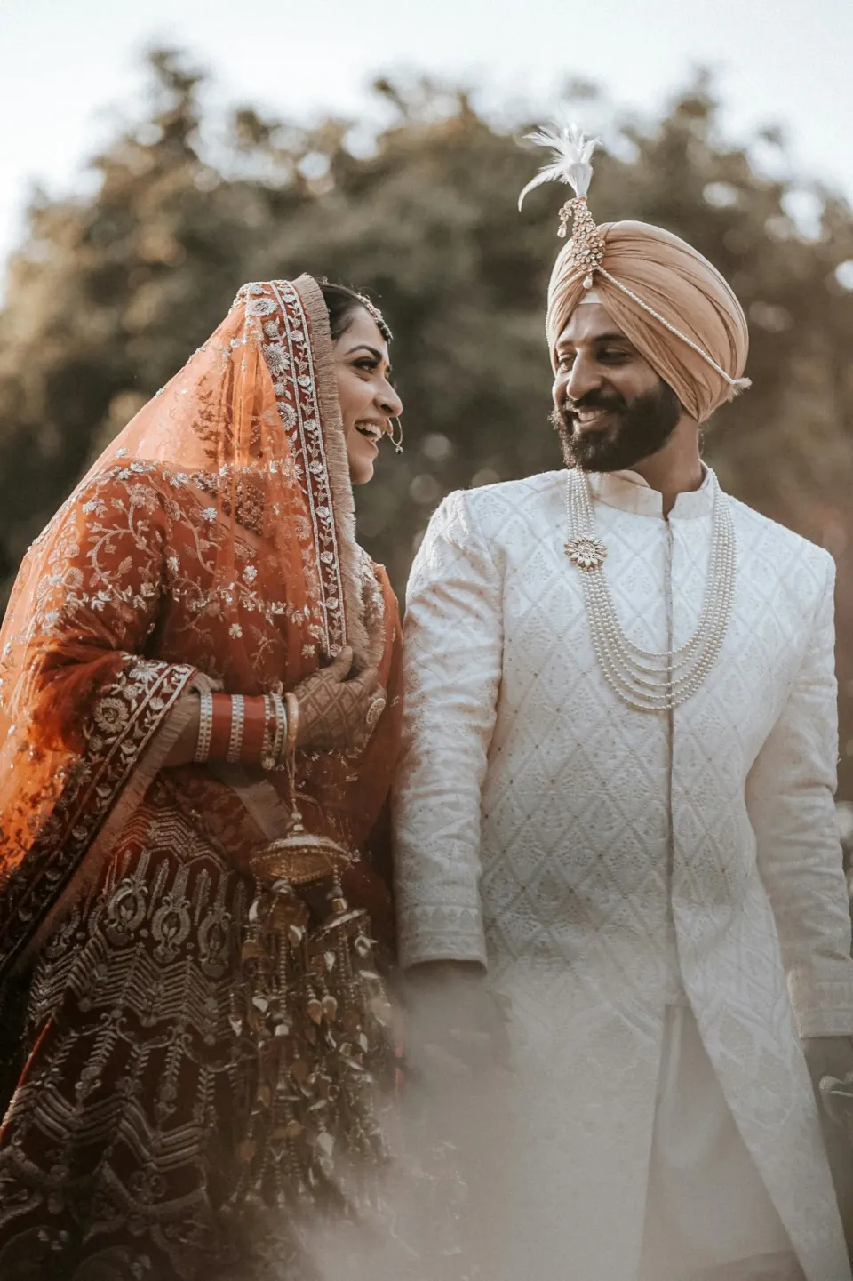 A Punjabi Sikh bride and groom smiling at each other, wearing traditional wedding attire